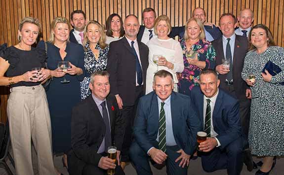 A group of 16 members of the agricultural alumni network at an event. All dressed smartly and smiling at the camera. 